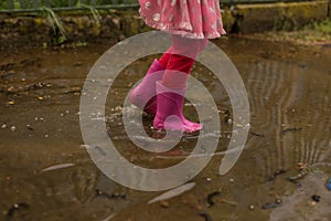 Playful little girl outdoor jump into puddle in pink boot after rain. Conceptual image.
