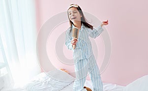 Playful little girl in pajama holding a hair brush like microphone singing imitates herself a real singer in the morning on the