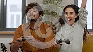 Playful middle eastern couple playing video games together at home, holding joysticks, tracking shot, slow motion
