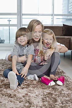 Playful mother with children sitting on rug in living room