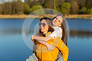 Playful mother giving daughter piggy back ride at spring lake shore