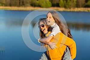 Playful mother giving daughter piggy back ride at spring lake shore