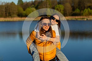 Playful mother giving daughter piggy back ride at spring lake shore