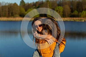 Playful mother giving daughter piggy back ride at spring lake shore