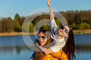 Playful mother giving daughter piggy back ride at spring lake shore