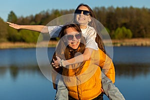 Playful mother giving daughter piggy back ride at spring lake shore