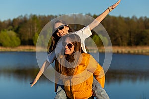 Playful mother giving daughter piggy back ride at spring lake shore