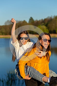 Playful mother giving daughter piggy back ride at spring lake shore