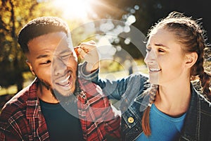 Playful, park and a girl pulling the ear of her boyfriend outdoor during summer for love while on a date. Couple, game