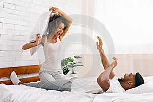 Playful pillow fight between smiling couple in bed