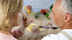 Playful senior couple cooking vegetable dinner at home, family togetherness