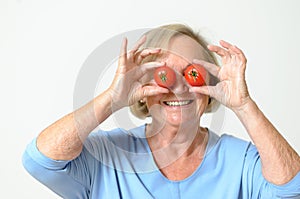 Playful senior lady holding tomatoes to her eyes