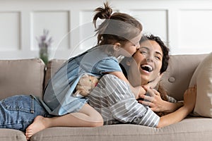 Playful small preschool daughter kissing mother`s cheek.