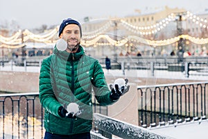 Playful smiling male juggles with snowballs throws them in air,