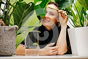 Playful smiling woman sitting behind a table in between big pots with plants