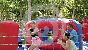 Playful sporty girl tied with rope to her friend competing to collect hoops on inflatable playground on sunny summer day