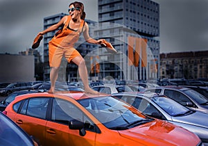 Playful stylish girl in orange overalls standing on car roof in the parking lot photo