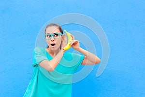 Funny Girl with Eyeglasses and Banana Phone on Blue Background