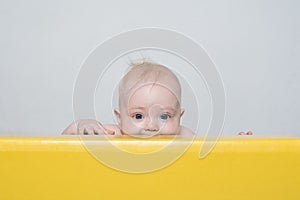 Playful surprised baby peeking out of playpen. Happy childhood