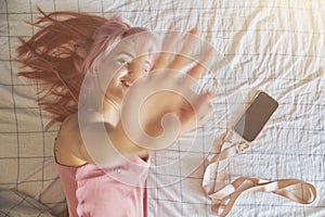 Playful woman hides from camera closing lens by palm on comfortable bed