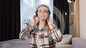 Playful woman dancing alone in green headphones in modern living room at home.