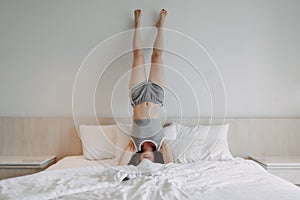 Playful woman is doing upside down pose on the bed.