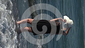 Playful woman standing in breaking waves and splashes on sandy beach during summer beach holidays