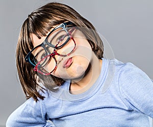 Playful young child trying several eyeglasses pouting and hesitating