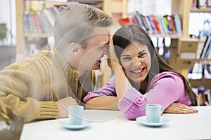 Playful young couple with coffee cups on desk in library