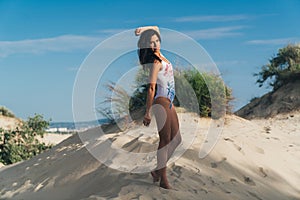 Playful young girl in a swimsuit enjoys her rest on the beach, whirls and rejoices, warms herself in the sun, the wind