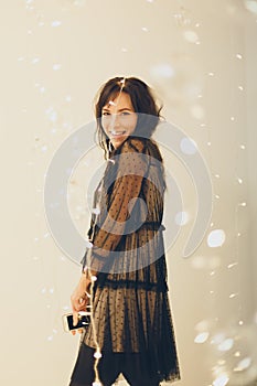 Playful young woman in cocktail dress staying smiling over lights background