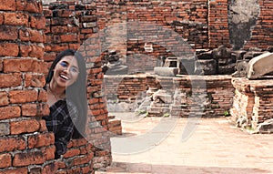 Playful young woman hiding behind brick wall while travelling ancient ruins tourist destination