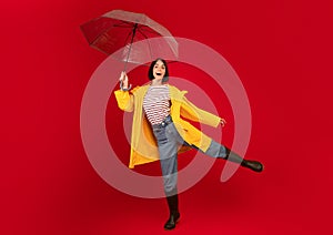 Playful young woman holding umbrella and having fun, laughing and looking at camera over red studio background