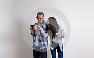Playful young woman laughing and distracting boyfriend while playing video game on smart phones. Cheerful young couple dressed in