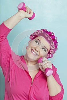 Playful young woman lifting weights over colored background