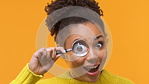 Playful young woman looking at camera through magnifying glass, curiosity search