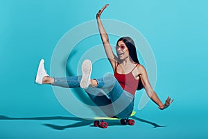 Playful young woman smiling while skateboarding against blue background