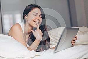 Playful young woman with tablet in hands on bed at home