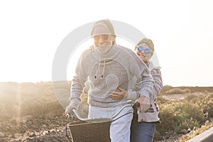 Playful and youthful senior caucasian peope couple enjoy a ride with bike together laughing and smiling -    concept of happiness