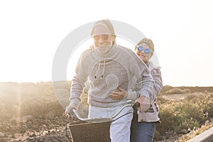 Playful and youthful senior caucasian peope couple enjoy a ride with bike together laughing and smiling -    concept of happiness photo
