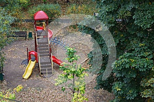 Playground for children.Ladder with yellow red slides bench sandbox surrounded by trees wet after the rain.