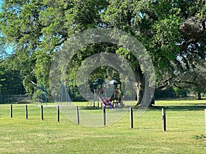 Playground equipment in a park with old oak trees.