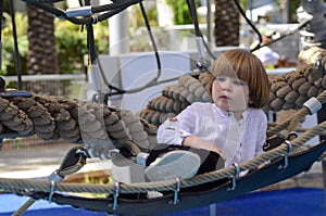 Playground. Grid for games. Rope park. A little boy sits in a hammock and shows his finger.r.