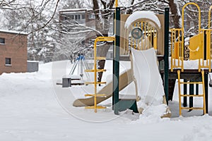 Playground with slide in park without children, covered with snow in winter season