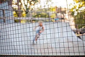 Playground with slides behind a mesh fence. Boys ride skateboards and scooters, blurred background