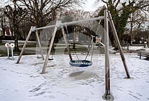 Playground swing and other equipment in snow covered grounds of Munkehagen park, Stavanger