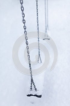 Playground swing set with steel chains covered in heavy snow, abandoned