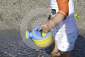 playing on the beach at the sunset time. baby playing with water on sea shore. closeup of the hand holding the watering