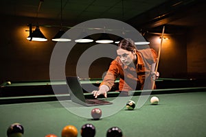 Playing billiards.Cute woman with balls and cue on a green pool table. Education pool billiard game using laptop
