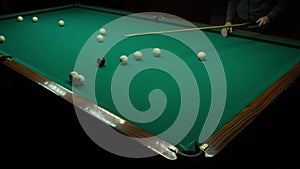 Playing billiards on a green table in a dark room. The man hits the balls with a cue and scores into the hole
